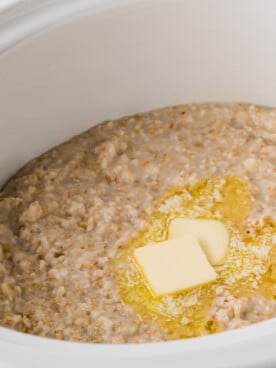 A crockpot of cooked oatmeal with butter melting on top.