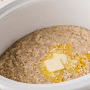 A crockpot of cooked oatmeal with butter melting on top.