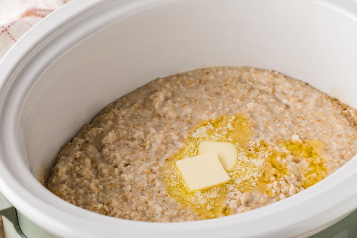 A crockpot of cooked oatmeal with butter melting on top.