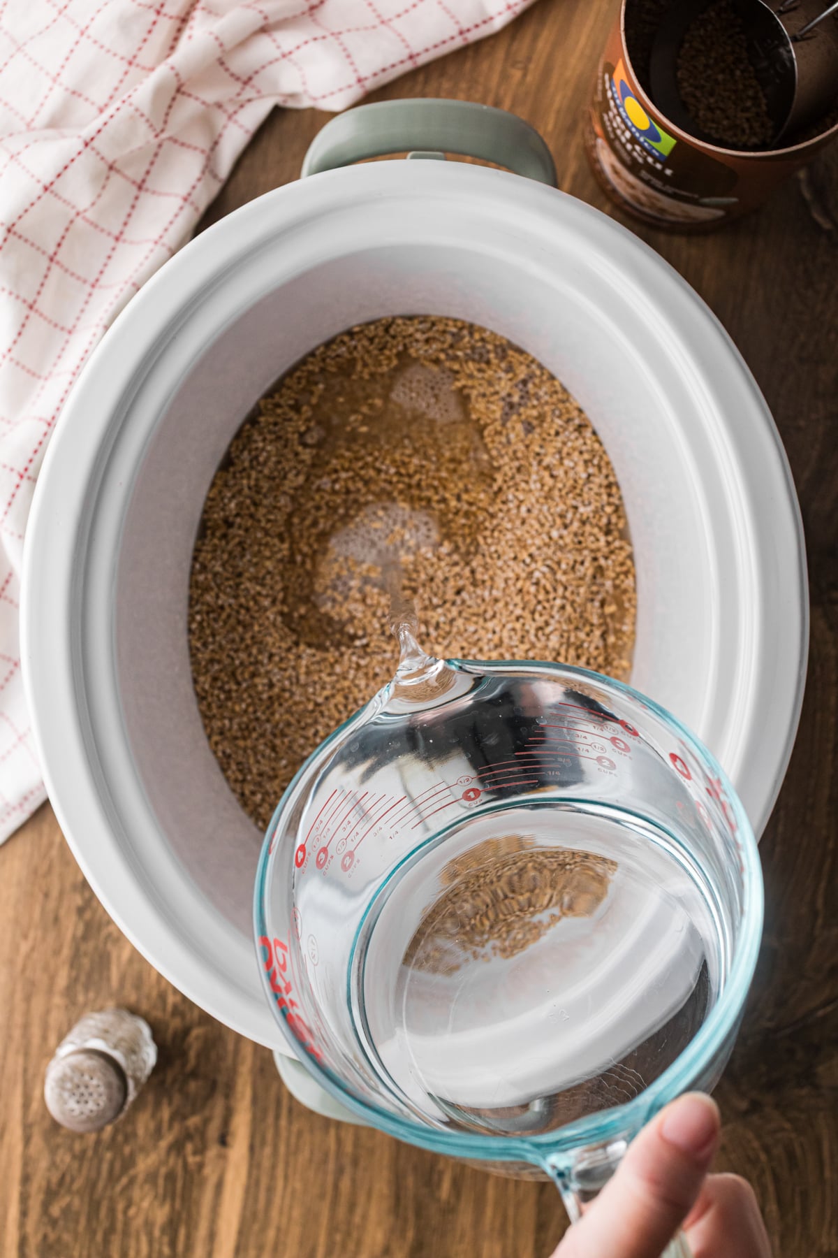 Pouring water into a crockpot with uncooked oats and salt.