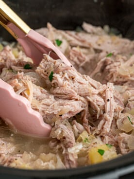 Tongs grabbing some pork and sauerkraut from a slow cooker.