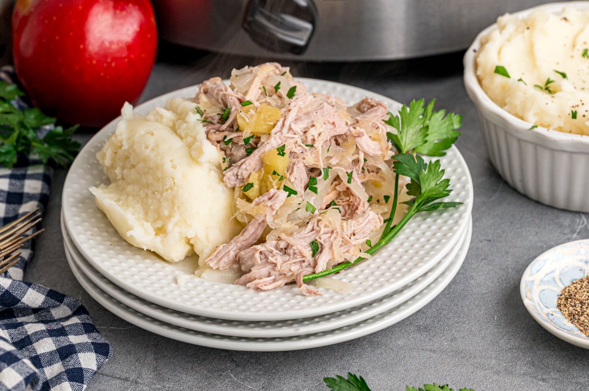 Pork and sauerkraut with mashed potatoes on a stack of plates.