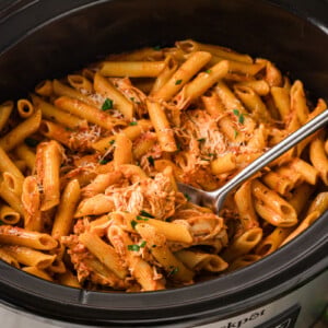 A large spoon scooping chicken pasta rosa from a slow cooker.