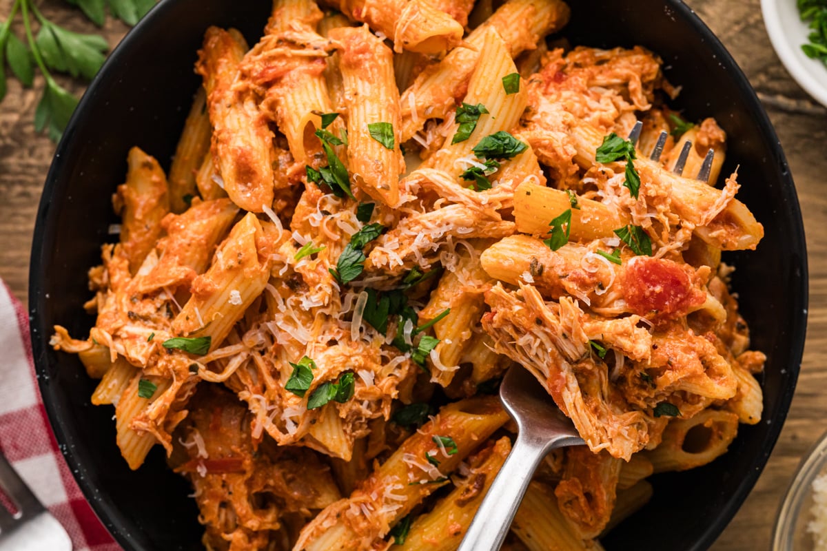 A fork grabbing chicken and pasta from a bowl.