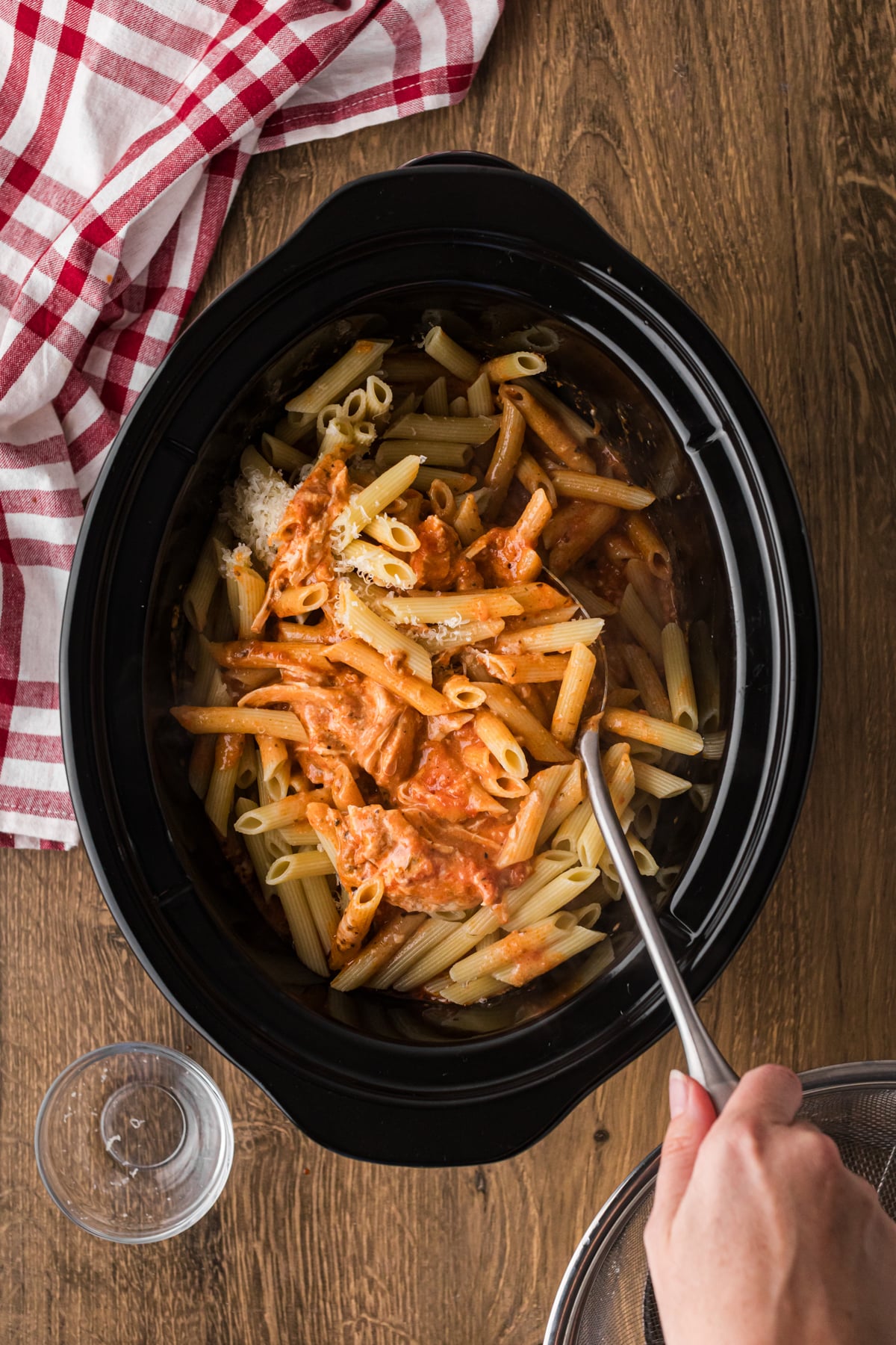 Stirring pasta, sauce, chicken, and cheese together in a slow cooker.