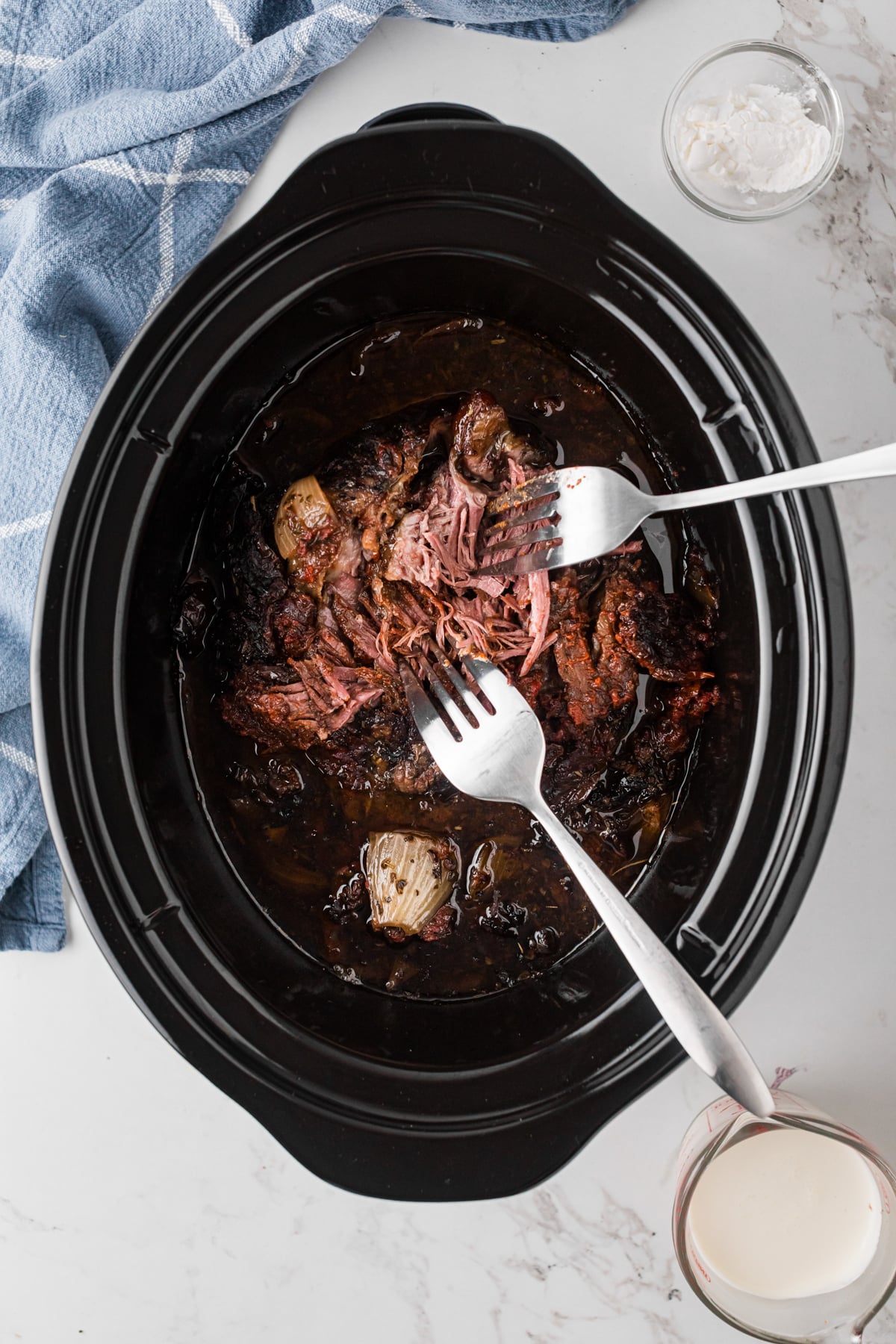 Shredded beef in a slow cooker with two forks.