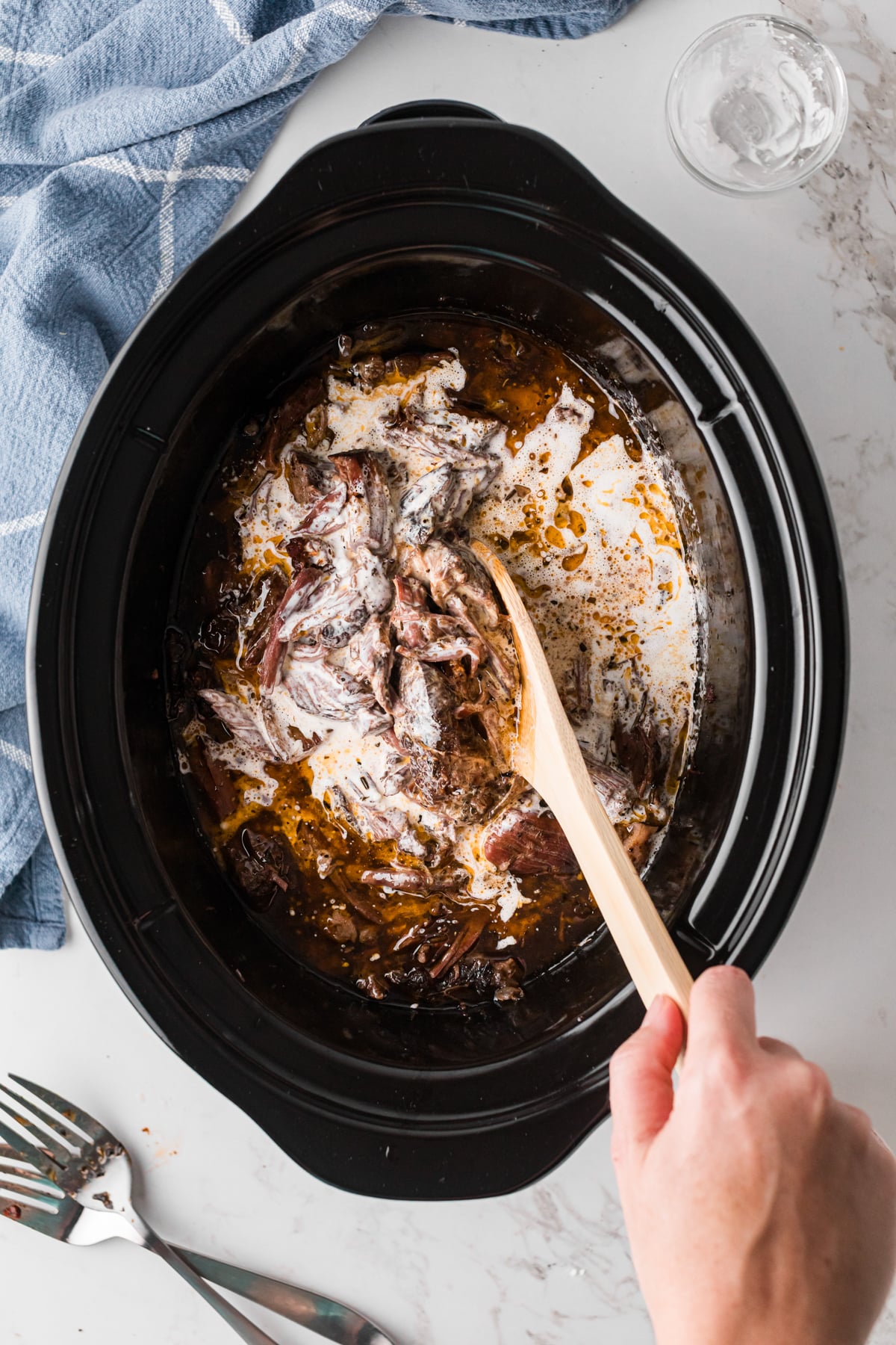 Stirring cornstarch and heavy cream into pot roast mixture in a crockpot.