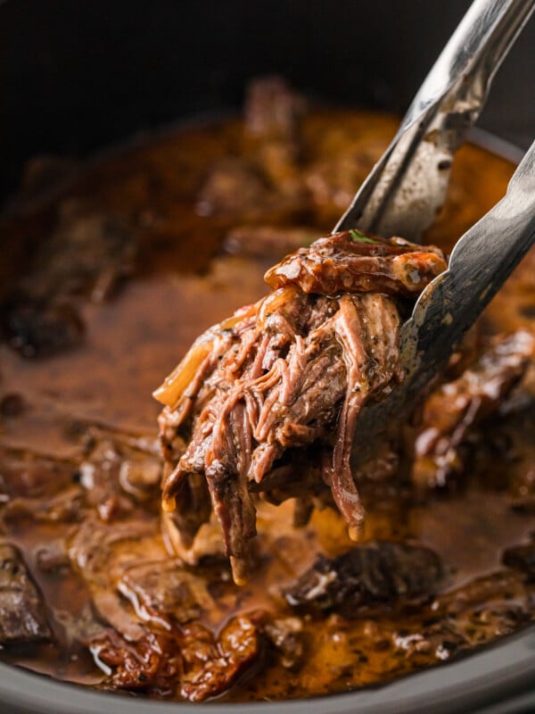 Tongs grabbing shredded pot roast from a crockpot.