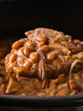 A wooden spoon holding a scoop of pork and beans over a crockpot.