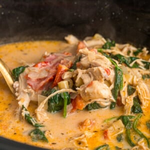 A large spoon scooping marry me chicken soup from a crockpot.