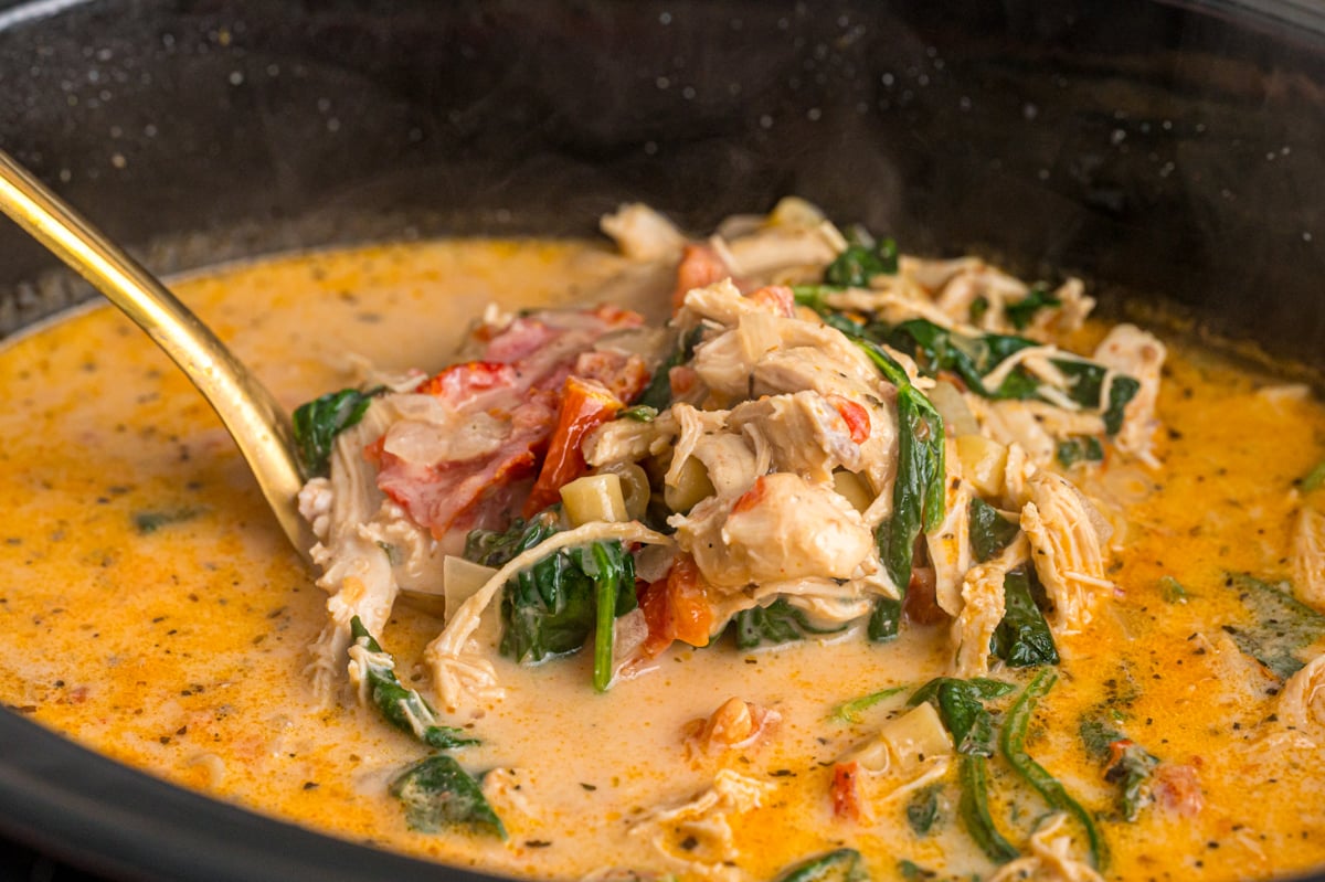 A large spoon scooping marry me chicken soup from a crockpot.