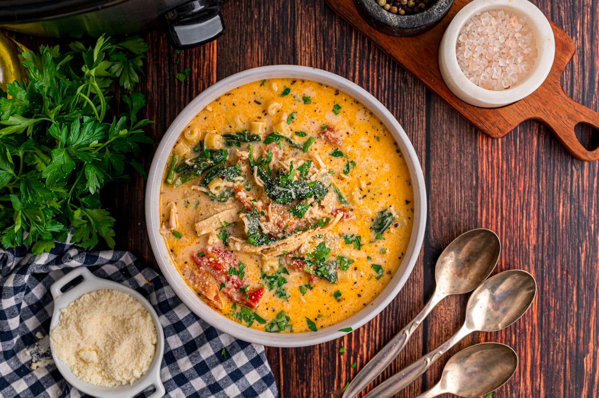 A serving of soup in a bowl with spoons and garnishes next to it.