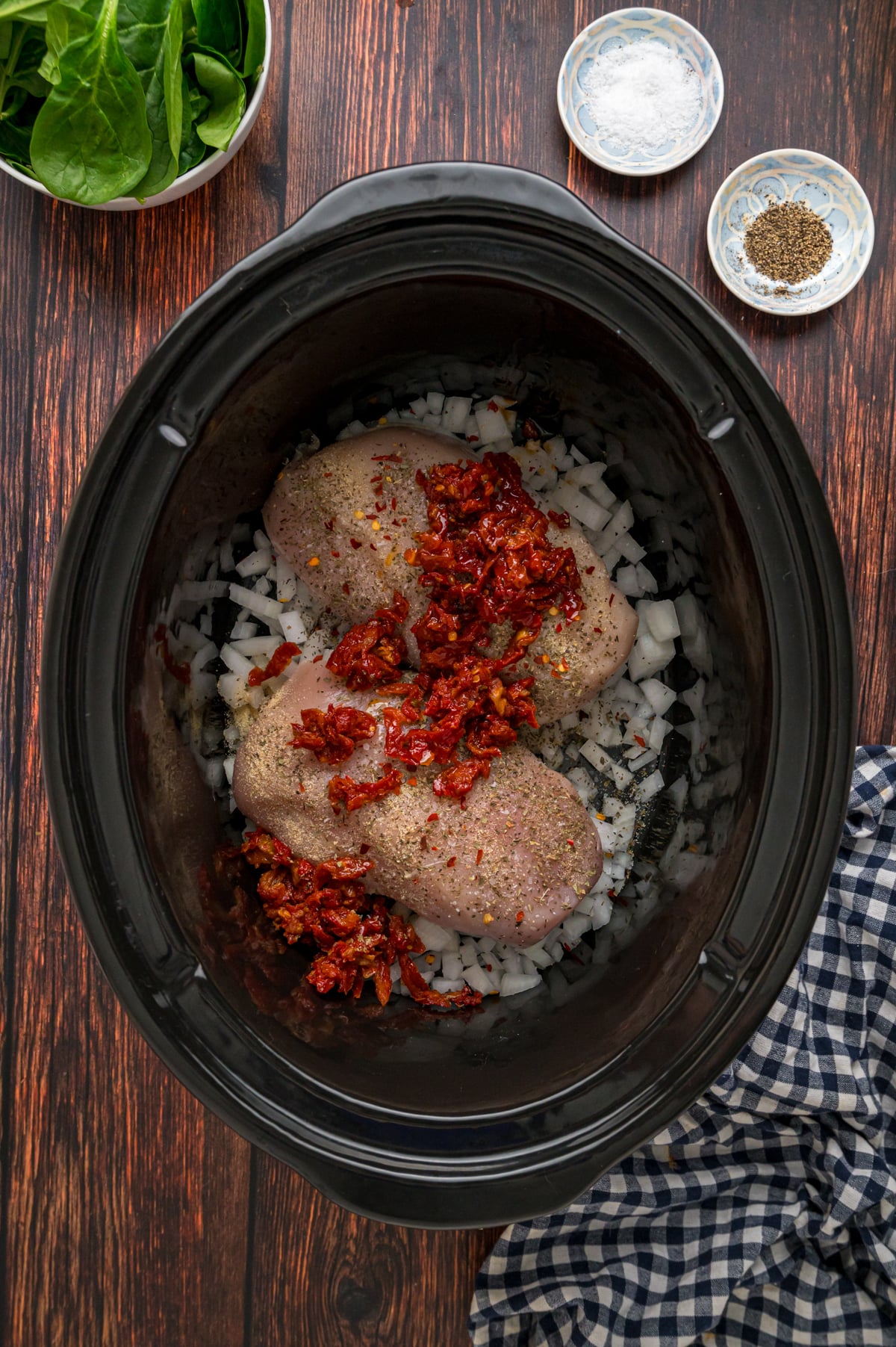 Seasoned chicken breasts, onion, and sun-dried tomatoes in a crockpot.