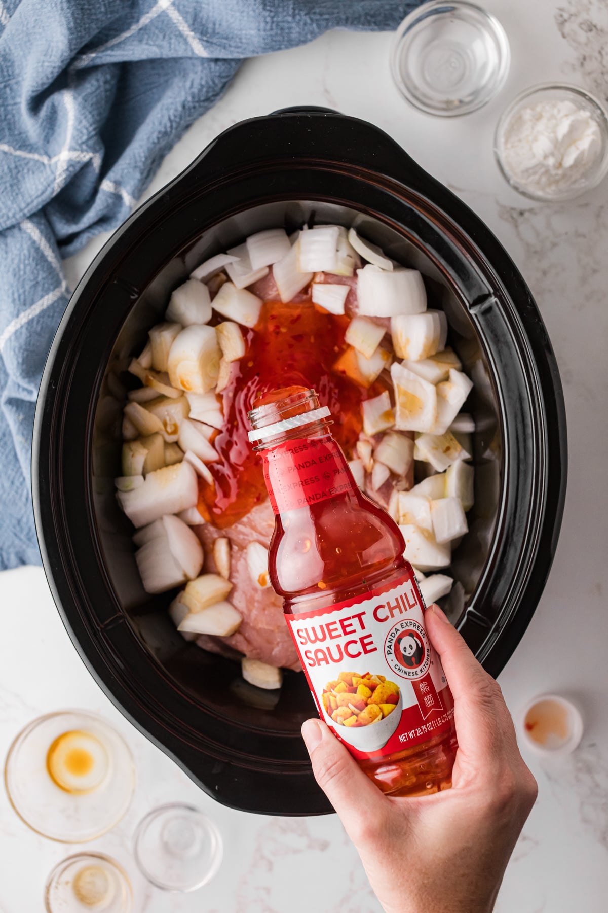 Sweet chili sauce being poured onto pork loin in a crockpot.