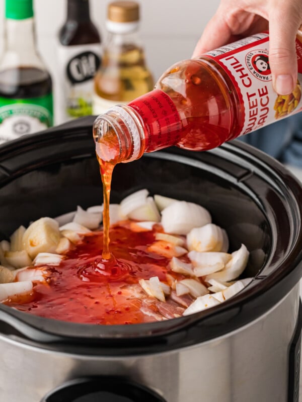 sweet chili being pour over pork in a slow cooker.