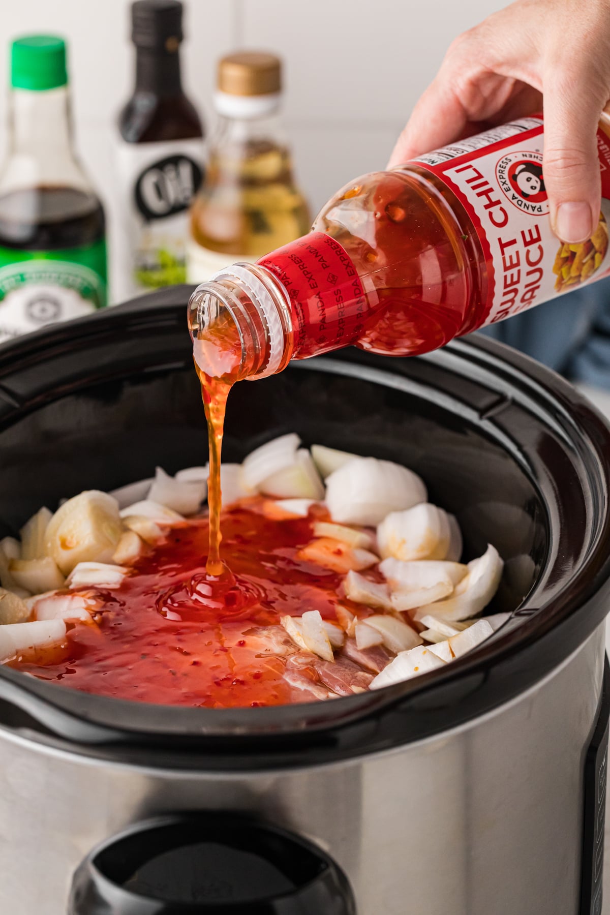 sweet chili being pour over pork in a slow cooker.