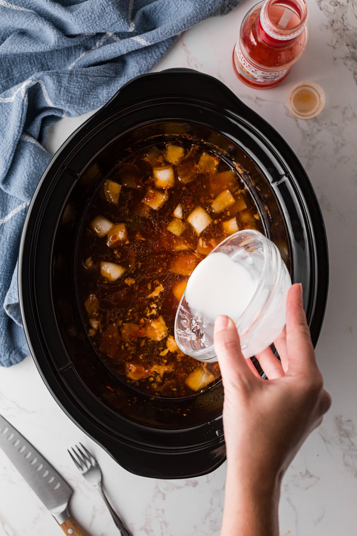 Pouring a cornstarch slurry into a crockpot to thicken a sauce.