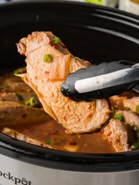 Tongs holding a piece of sweet chili pork over a crockpot.