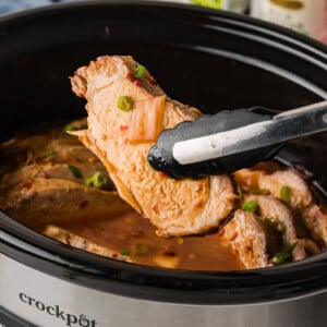 Tongs holding a piece of sweet chili pork over a crockpot.