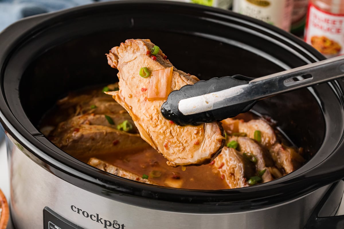 Tongs holding a piece of sweet chili pork over a crockpot.