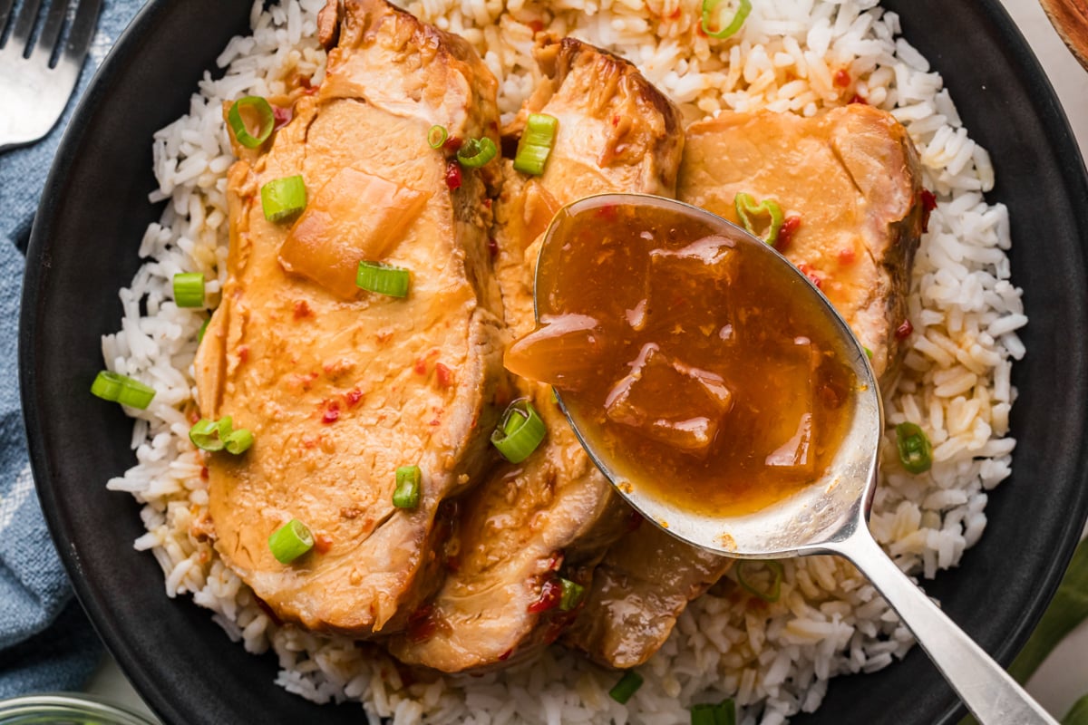 A spoon about to drizzle sweet chili sauce over three pieces of cooked pork over rice.