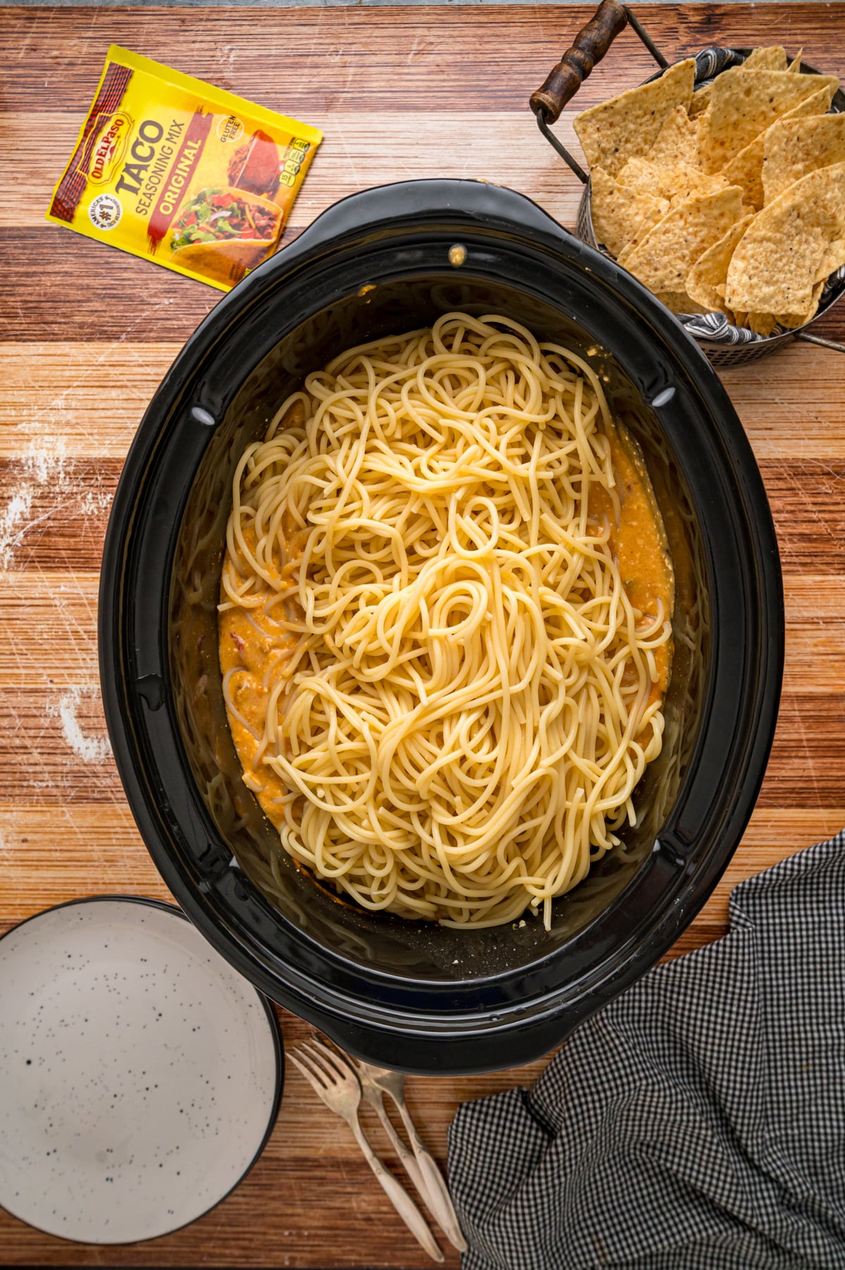 Cooked spaghetti added to a creamy mixture with chicken in a crockpot.