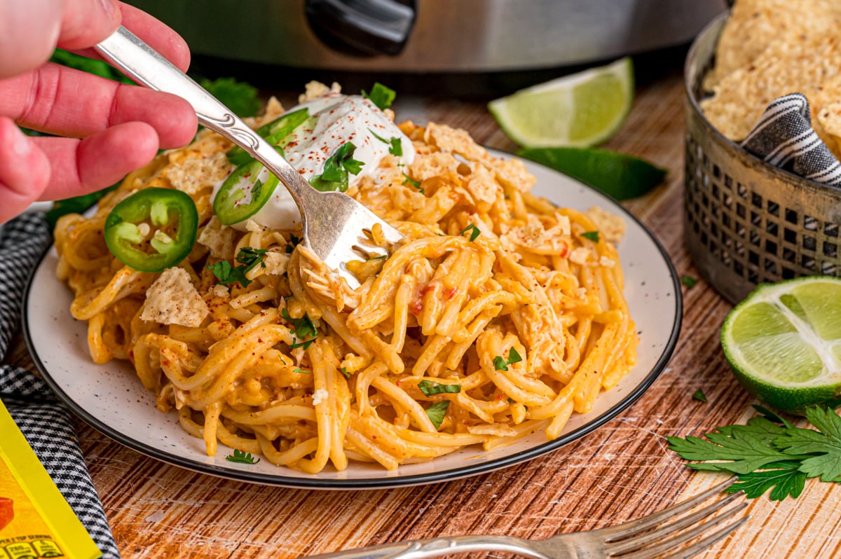 A hand grabbing a forkful of chicken taco spaghetti from a plate.