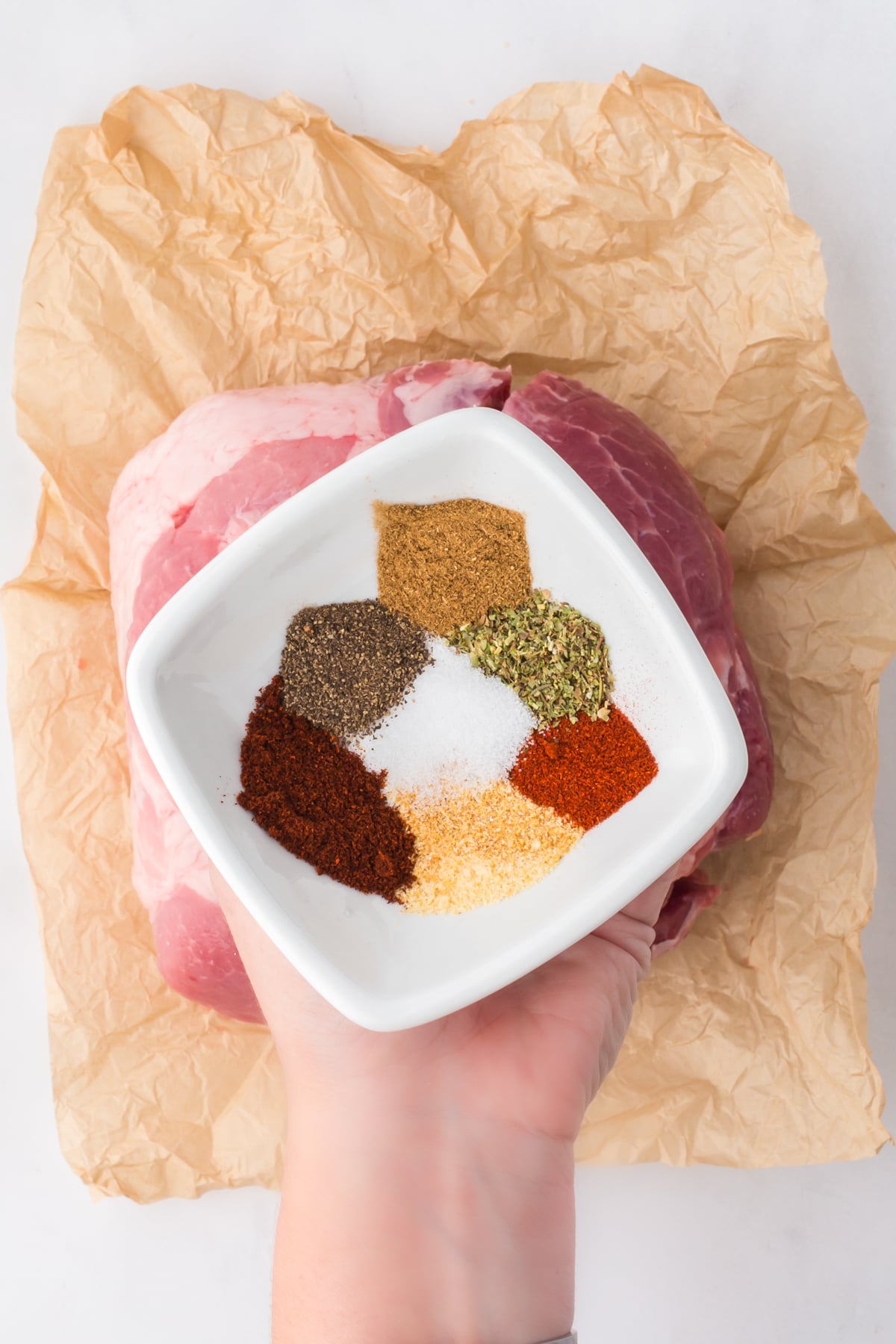 A hand holding a white bowl of seasonings.
