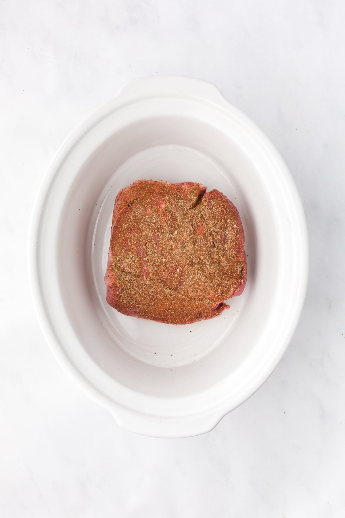 Seasoned pork placed in the bottom of a slow cooker.