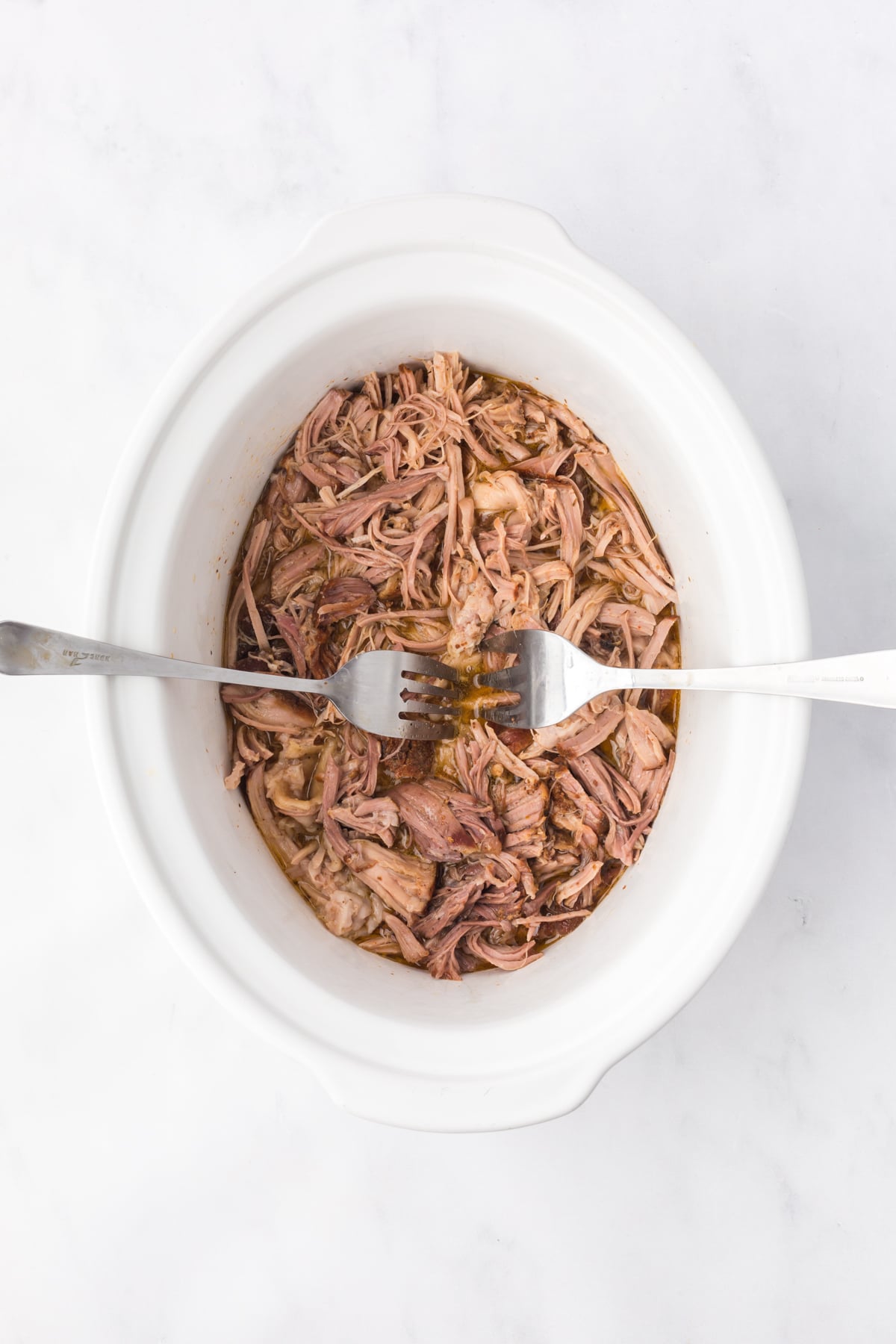 A crockpot of shredded pork with two forks in it.