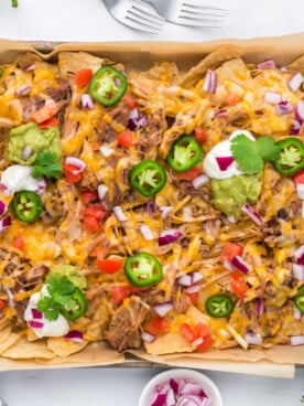 A sheet pan with pulled pork nachos, melted cheese, and a variety of toppings.