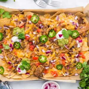 A sheet pan with pulled pork nachos, melted cheese, and a variety of toppings.