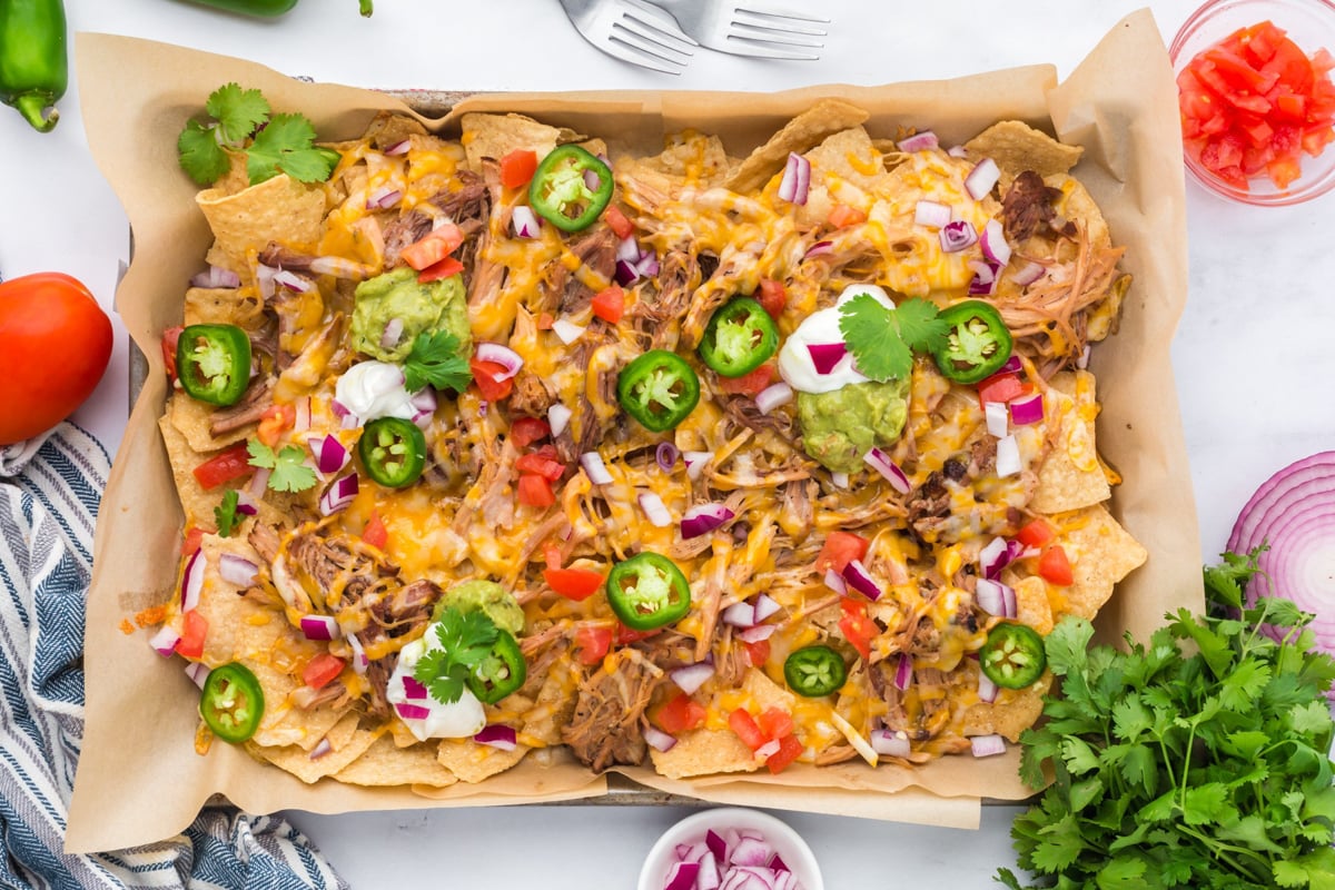 A sheet pan with pulled pork nachos, melted cheese, and a variety of toppings.