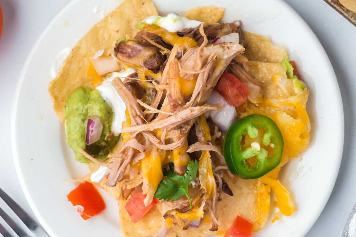 A close-up of a serving of nachos with pulled pork, cheese, and colorful toppings.