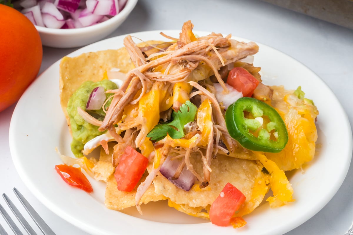 A plate of nachos topped with shredded pork, melted cheese, and a variety of toppings.