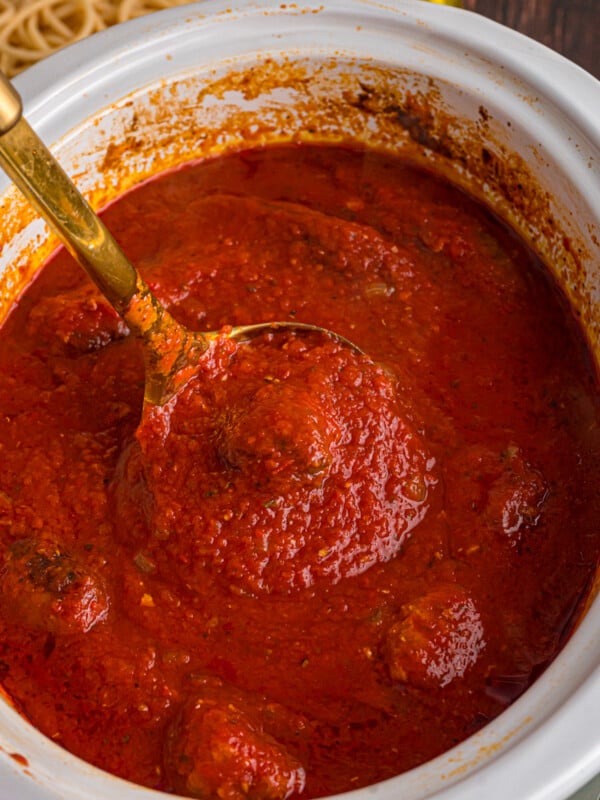 A ladle holding a scoop of Sunday sauce over a slow cooker.