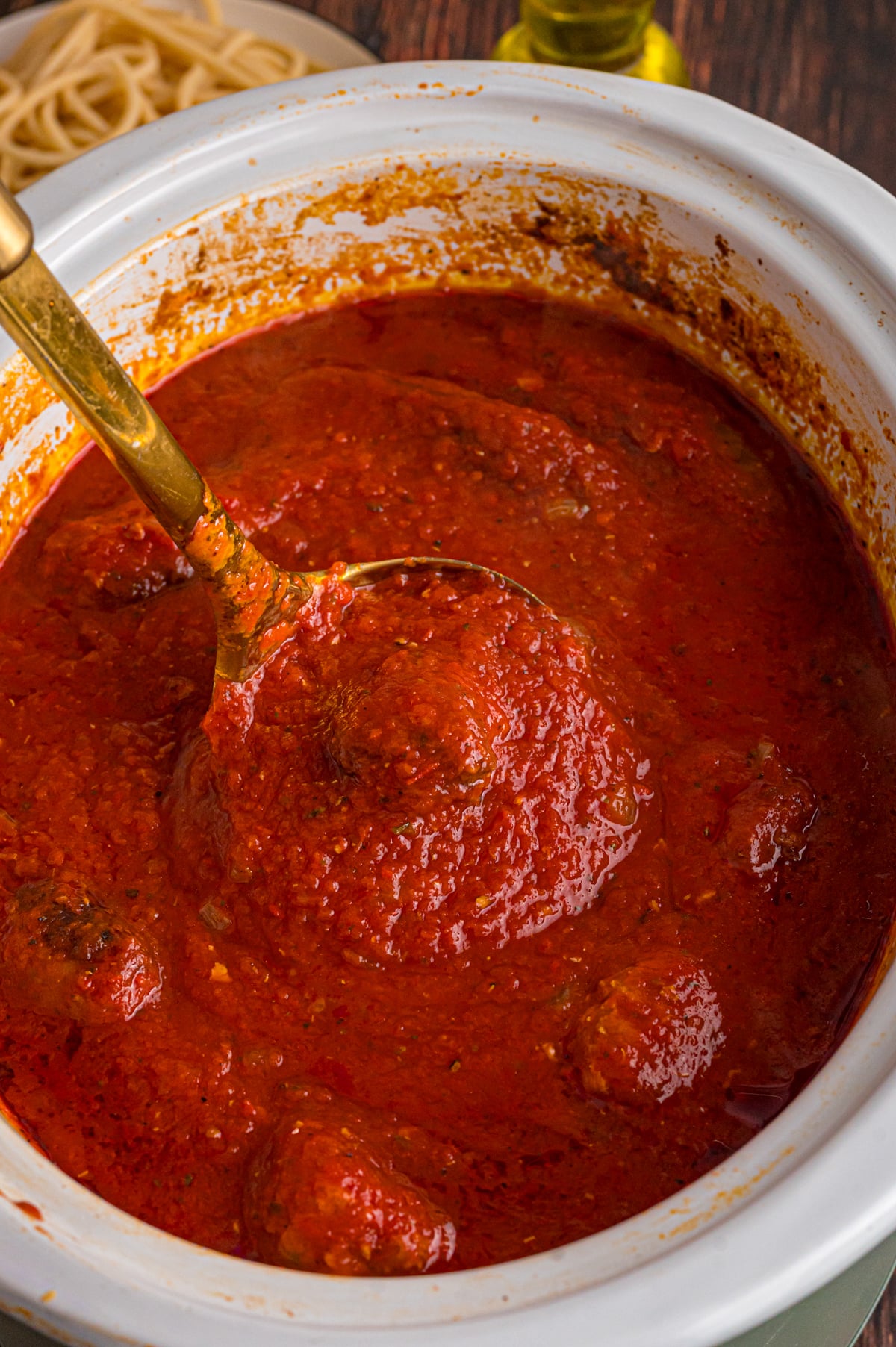 A ladle holding a scoop of Sunday sauce over a slow cooker.