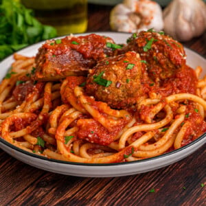 A dish of spaghetti topped with sausage and meatballs in tomato sauce.