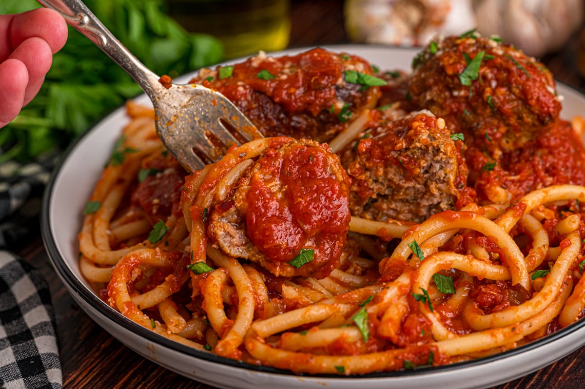 A fork grabbing a meatball wrapped in spaghetti from a dish.