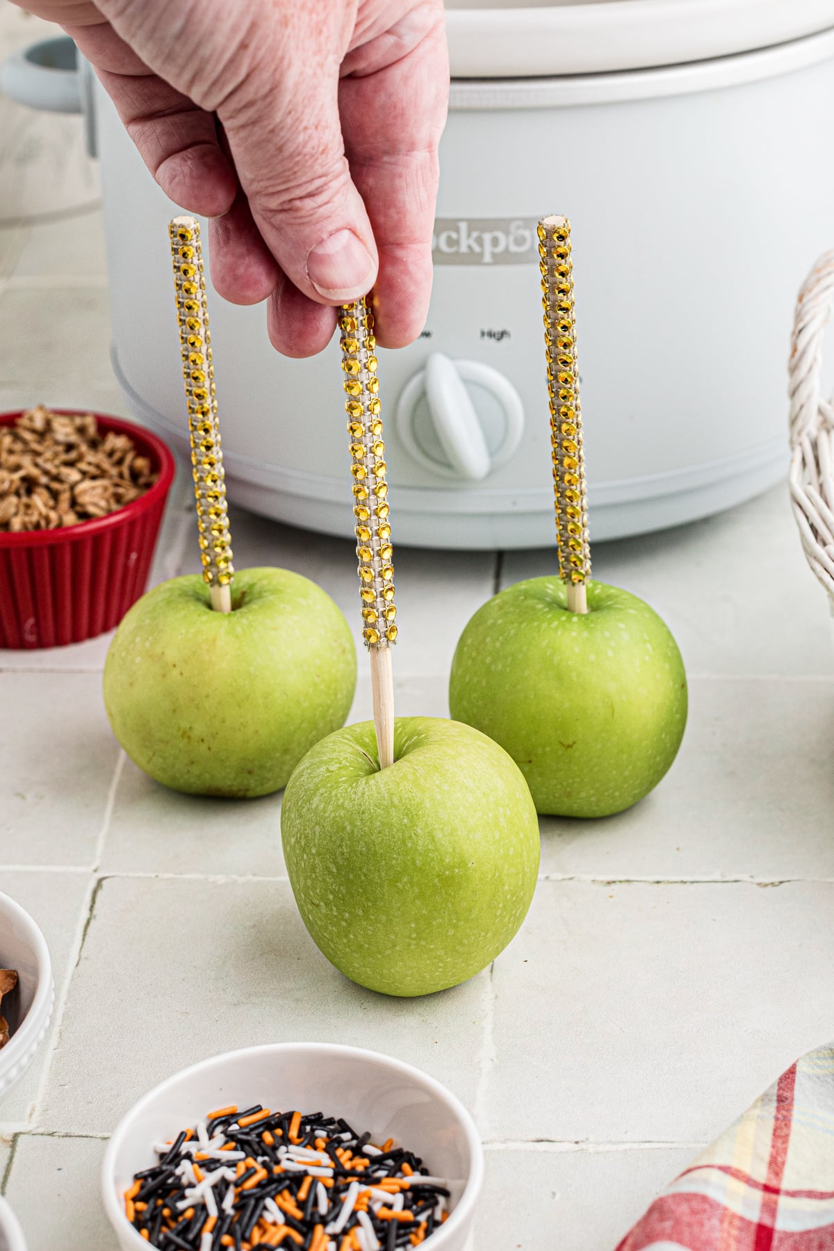 A handing placing sticks into the tops of apples.