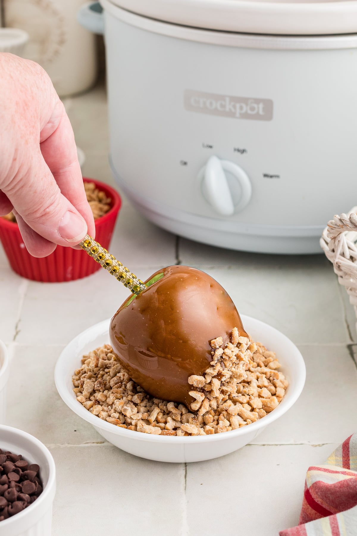 A hand rolling a caramel dipped apple into chopped peanuts.