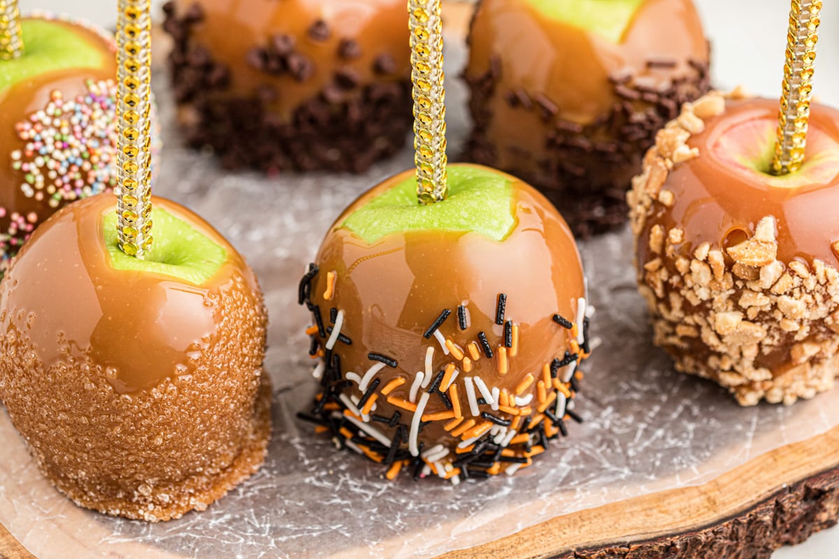 Close-up of caramel dipped apples with various toppings on a wooden board.