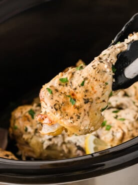 Tongs grabbing a chicken drumstick from a crockpot.